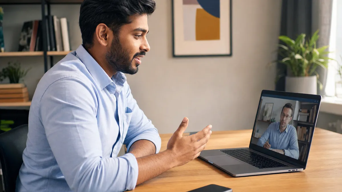 Job candidate at a laptop during a video interview, gesturing as she speaks, with a phone resting screen-down on the desk beside her