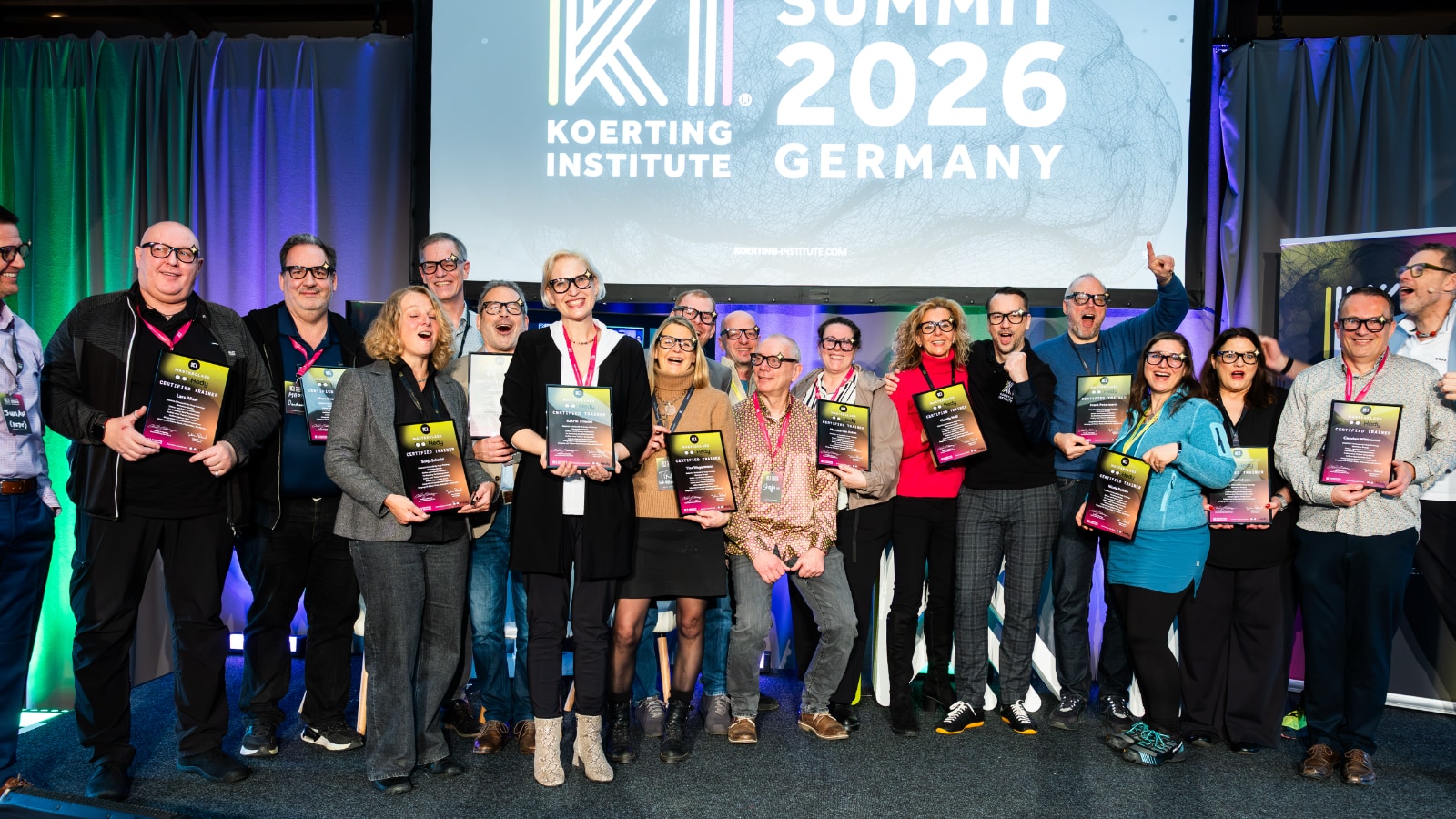Grupo de formadores certificados sosteniendo certificados en el escenario del KI Summit 2026 en Alemania