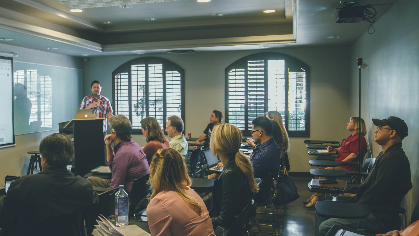 Ponente presentando ante un público sentado en una sala con ventanas de arco